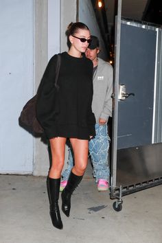 a woman in black sweater and boots walking down the street with her hand on her hip