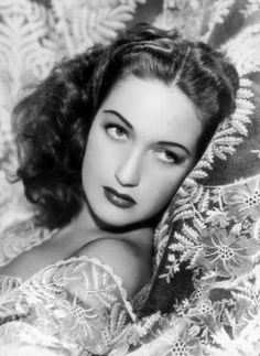 an old black and white photo of a woman laying on a bed covered in lace