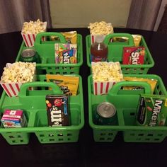 four green baskets filled with movie snacks and sodas on top of a black table