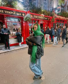 a woman with a green scarf on her head standing in front of the temple bar