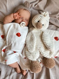 a baby sleeping next to a teddy bear on top of a white blanket with red hearts