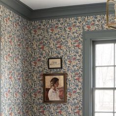 a painting hangs on the wall next to a window in a room with floral wallpaper