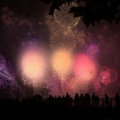 fireworks are lit up in the night sky with people standing around looking at them and taking pictures