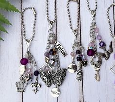 several different necklaces with charms attached to them on a white wooden table next to a plant