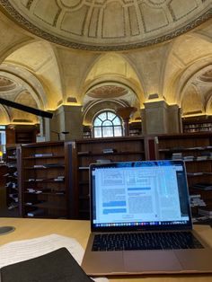 an open laptop computer sitting on top of a wooden desk in a library filled with books