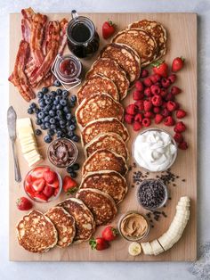 pancakes, strawberries, bananas, blueberries and other foods are arranged on a cutting board