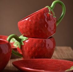 three red ceramic strawberry cups and saucers on a wooden table with one sitting in the middle