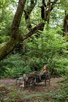 a man and woman sitting on top of a green chair under a tree in the woods