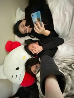 two women laying on top of a bed next to a hello kitty stuffed animal toy