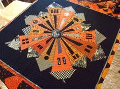 a quilted table topper with an orange and black design on the center piece