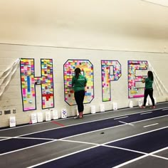 two women standing in front of a wall that has letters on it and the word hope spelled out