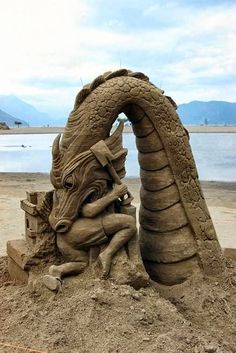 a sand sculpture of a dragon and a woman on the beach