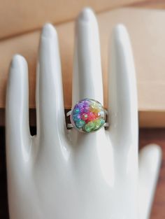 How pretty is this statement ring? Rainbow crystal shimmering faceted jewels are nestled inside crystal clear resin in this adjustable (one size fits all) but also super durable 10mm stainless steel bands. This is an absolutely stunningly pretty piece. Reminds me of spring flowers! have an idea for this, but in a different color? customs are available, lead times are 7-10 days, but your vision is our inspiration! message us for details! *as our products are all made by hand, slight variations in texture/pattern/specific color hues, etc. is possible, please remember this as you order!  i am a complete perfectionist and try to ensure every single piece is completely perfect; however with our dedication to using our hands, hand tools, and very light power tools, sometimes minor imperfections Multicolor Crystal Rings For Gift, Adjustable Iridescent Jewelry Ring, Adjustable Iridescent Rings, Adjustable Iridescent Ring, Handmade Adjustable Iridescent Crystal Ring, Adjustable Faceted Crystal Ring, Adjustable Crystal Ring For Gift, Iridescent Resin Round Jewelry, Adjustable Multicolor Crystal Ring