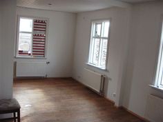 an empty room with hard wood floors and white walls, two windows on the far wall