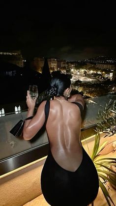 a woman standing on top of a balcony holding a wine glass in one hand and looking at the city