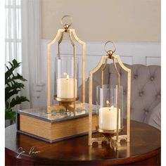 two candles sitting on top of a wooden table next to a book and glass container