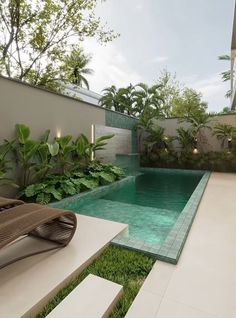 an outdoor swimming pool surrounded by greenery next to a patio with chaise lounges