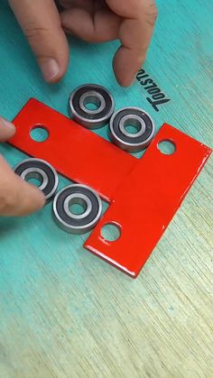 two hands are working on an object that looks like a red box with four bearing units