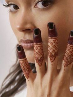 a woman holding her hands up to her face with henna tattoos on it's fingers