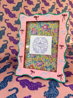 a small pink frame with an ornate design on the front and bottom, sitting on a patterned surface