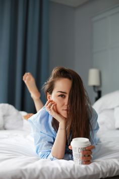 a woman laying on top of a bed with a cup of coffee in her hand