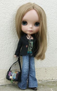 a doll with blonde hair holding a handbag next to a white wall and cement floor