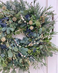 a wreath is hanging on the side of a white door with greenery and berries