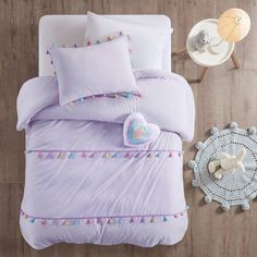 a bed with purple sheets and pillows next to a white teddy bear on the floor