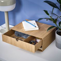 a wooden desk with glasses, notebook and pen on it next to a plant in a pot