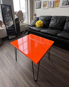 an orange table sitting in the middle of a living room next to a black couch