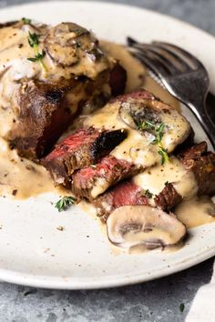 a white plate topped with meat covered in gravy next to a knife and fork