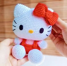 a hand holding a hello kitty crochet doll with a red bow on it's head