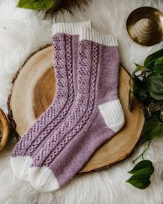 two pairs of purple socks sitting on top of a white rug next to a wooden slice