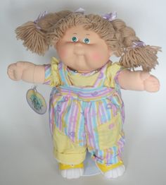 a doll with blonde hair and blue eyes wearing yellow overalls on a white background