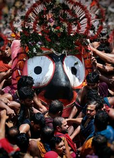 a group of people standing around a large mask with flowers on it's face