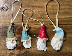 three ceramic ornaments are hanging on a wooden surface, one is wearing a red hat and the other has a blue cap