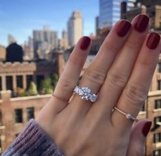 a woman's hand holding an engagement ring in front of a cityscape