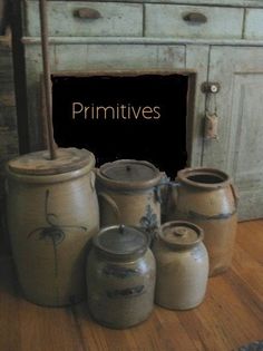 primitive jars and containers are sitting on the floor in front of an old cabinet with a primitive stick sticking out of it