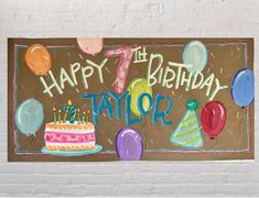 a happy birthday sign with balloons and a cake on the table in front of it