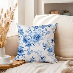 a blue and white flowered pillow sitting on top of a couch next to a cup