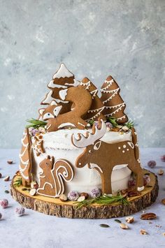 a decorated christmas cake with gingerbread and icing on a tree stump, surrounded by nuts