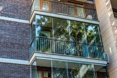 an apartment building with glass balconies and trees in the window, on a sunny day