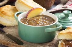 a bowl of soup and some bread on a cutting board with an apple in it