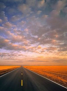 an empty road with no cars on it in the middle of nowhere under a cloudy sky