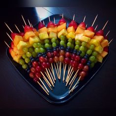 fruit skewers arranged in the shape of a heart on a black platter