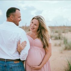 a pregnant couple standing in the desert smiling at each other's eyes and laughing