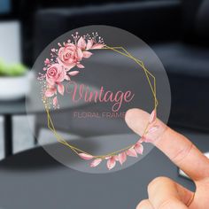 a person holding up a round sticker that says vintage floral frame with pink flowers on it