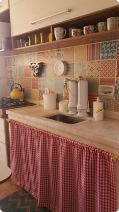 the kitchen counter is covered with red and white checkered curtains, which are hanging above the sink