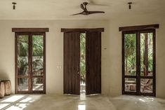 an empty living room with three doors and two windows that look out onto the jungle