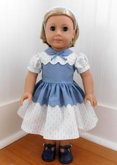 a doll with blonde hair wearing a blue and white dress is standing in front of a wall